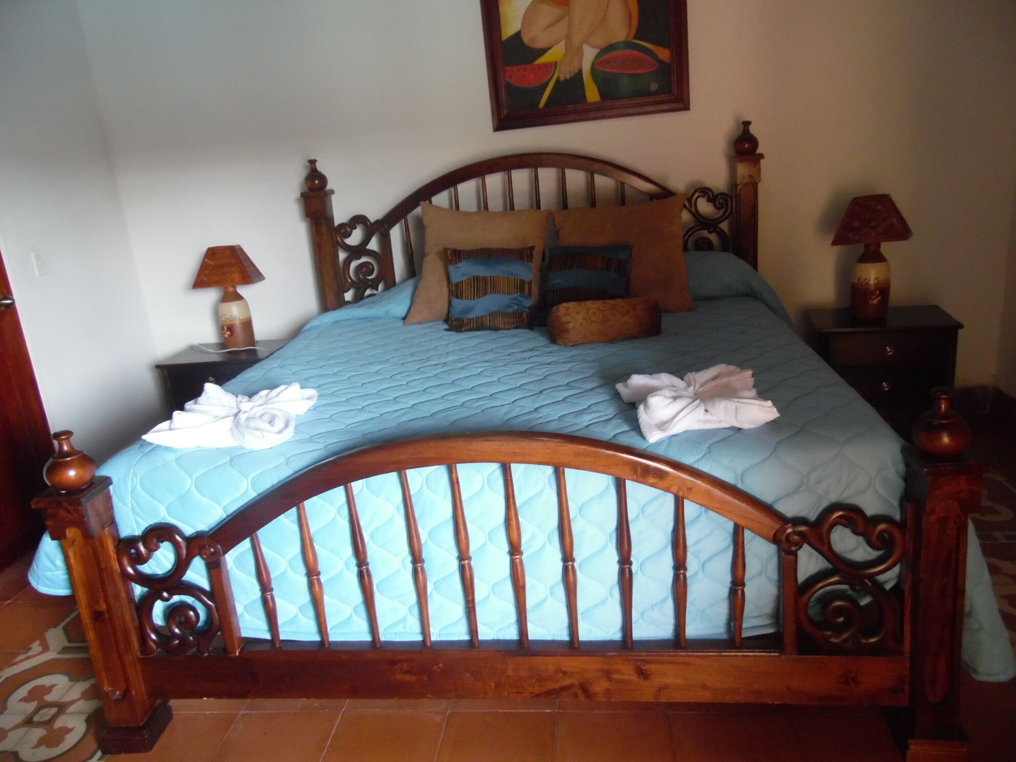 Un lit avec une tête de lit en bois, une courtepointe bleue et plusieurs oreillers. Il y a un tableau accroché au mur au-dessus du lit.