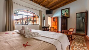 Habitación de hotel con una cama grande, techo de madera, ventana con vistas al exterior, puerta de madera y una silla.