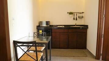 A compact kitchen with a microwave, a sink, and a small countertop. There is a dining table with chairs and a rug on the floor.