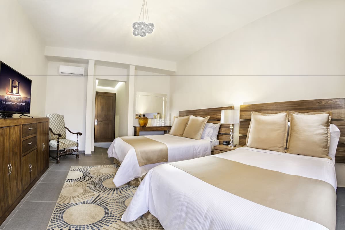 A hotel room with two beds, a TV, a wooden dresser, and a patterned rug.
