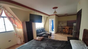 A bedroom with a large bed, a TV mounted on the wall, a sofa, and a dining area with chairs. - Hotel Savoy  (La Paz)