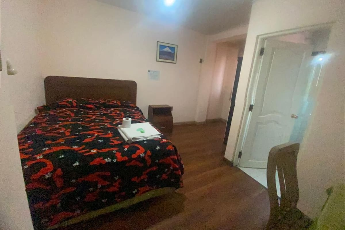 A bedroom with a bed, a chair, a door, and a small table.