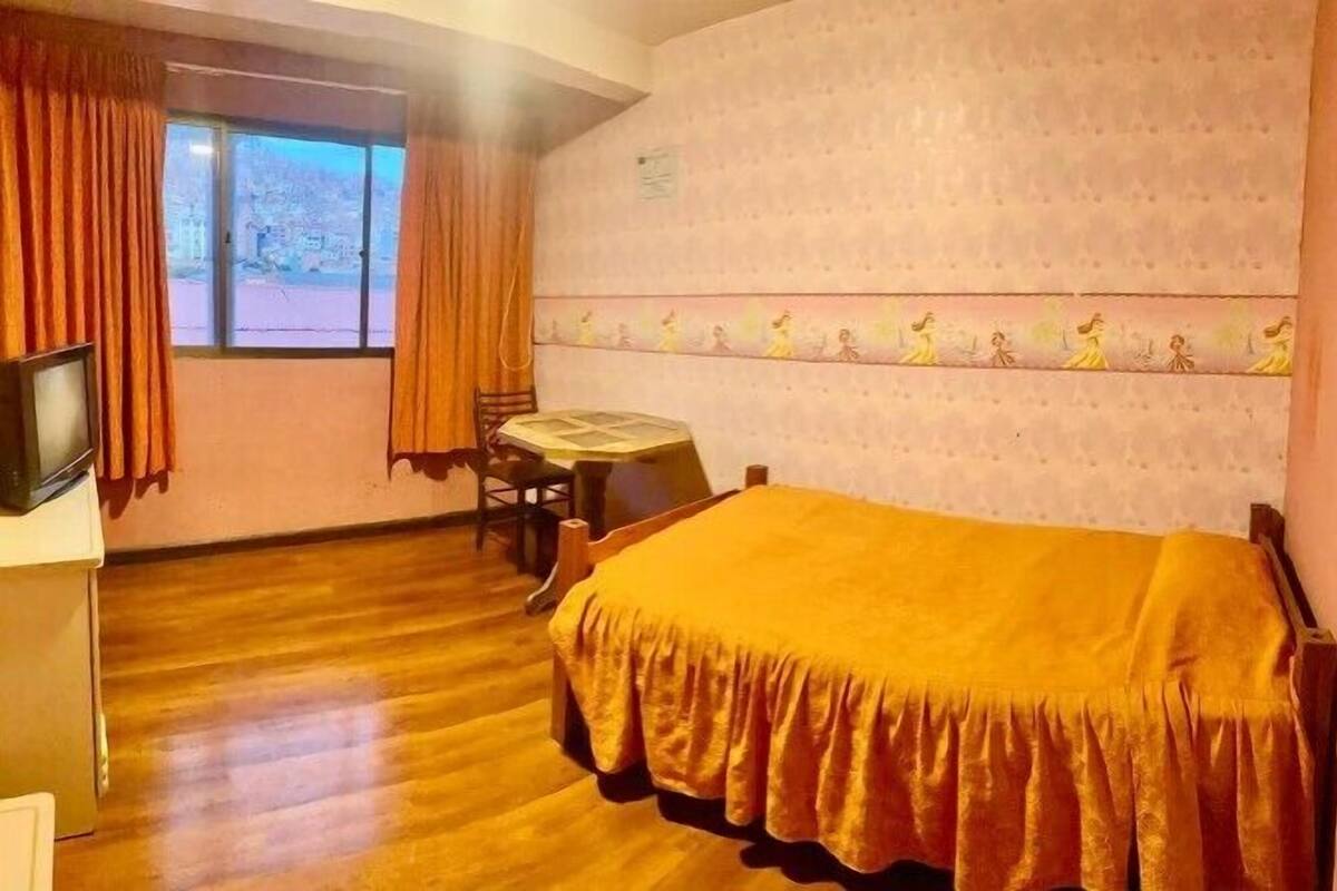 A hotel room with a bed, a desk, a chair, a television, and a window with curtains.