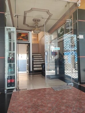 Un hall d’hôtel avec un sol carrelé, un escalier et une porte en verre sur laquelle est apposée une enseigne.