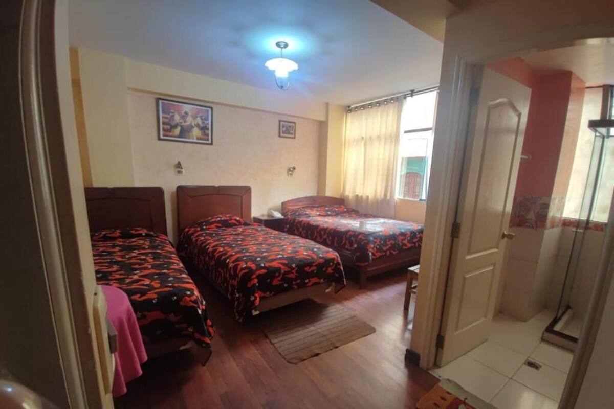 A room with three beds, a ceiling light, a door, and a window with curtains.