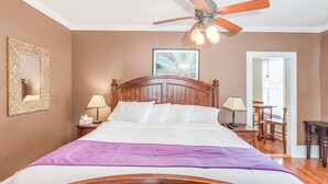 A bedroom with a wooden bed, a ceiling fan, a framed mirror, and a bedside table with a lamp. - The Heirloom Inn (Mount Dora)