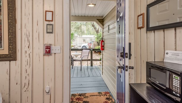 A doorway leading to a porch with a fire extinguisher, a doormat, and a microwave on a counter. - The Heirloom Inn (Mount Dora)