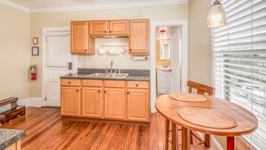 A kitchen with wooden cabinets, a granite countertop, and a dining area with a wooden table and chairs. - The Heirloom Inn (Mount Dora)