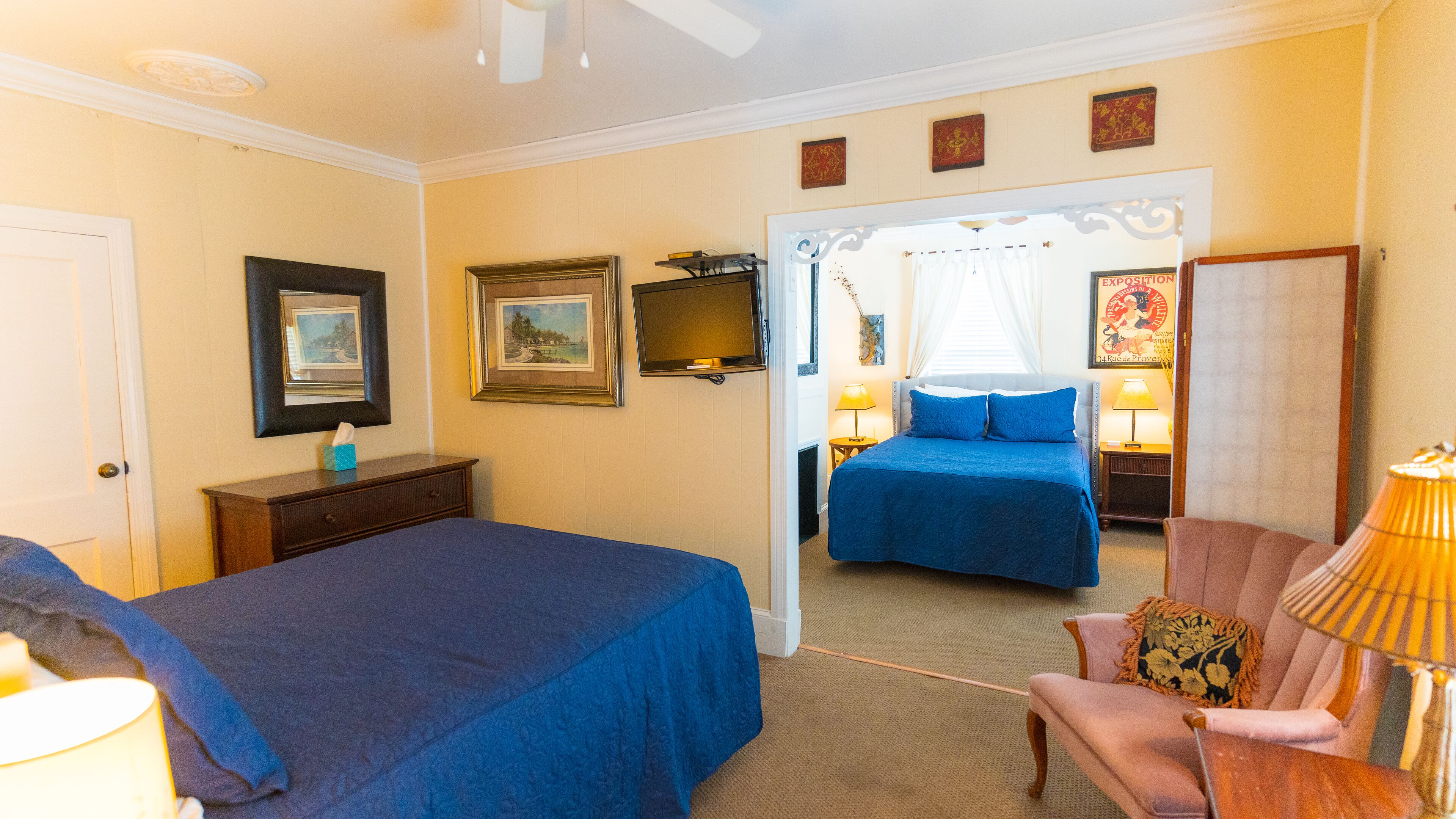 A hotel room with two beds, a desk, a chair, and a TV.