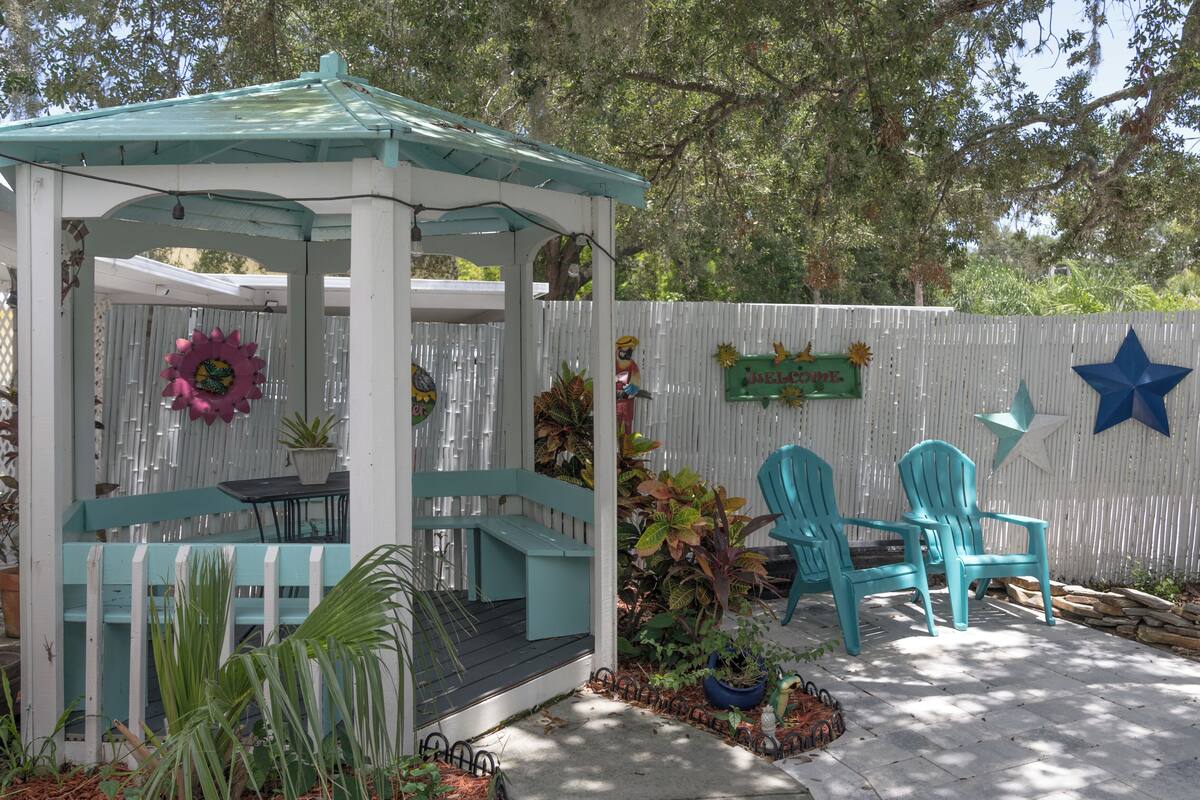 A gazebo with a green roof, a white fence, and two turquoise chairs.