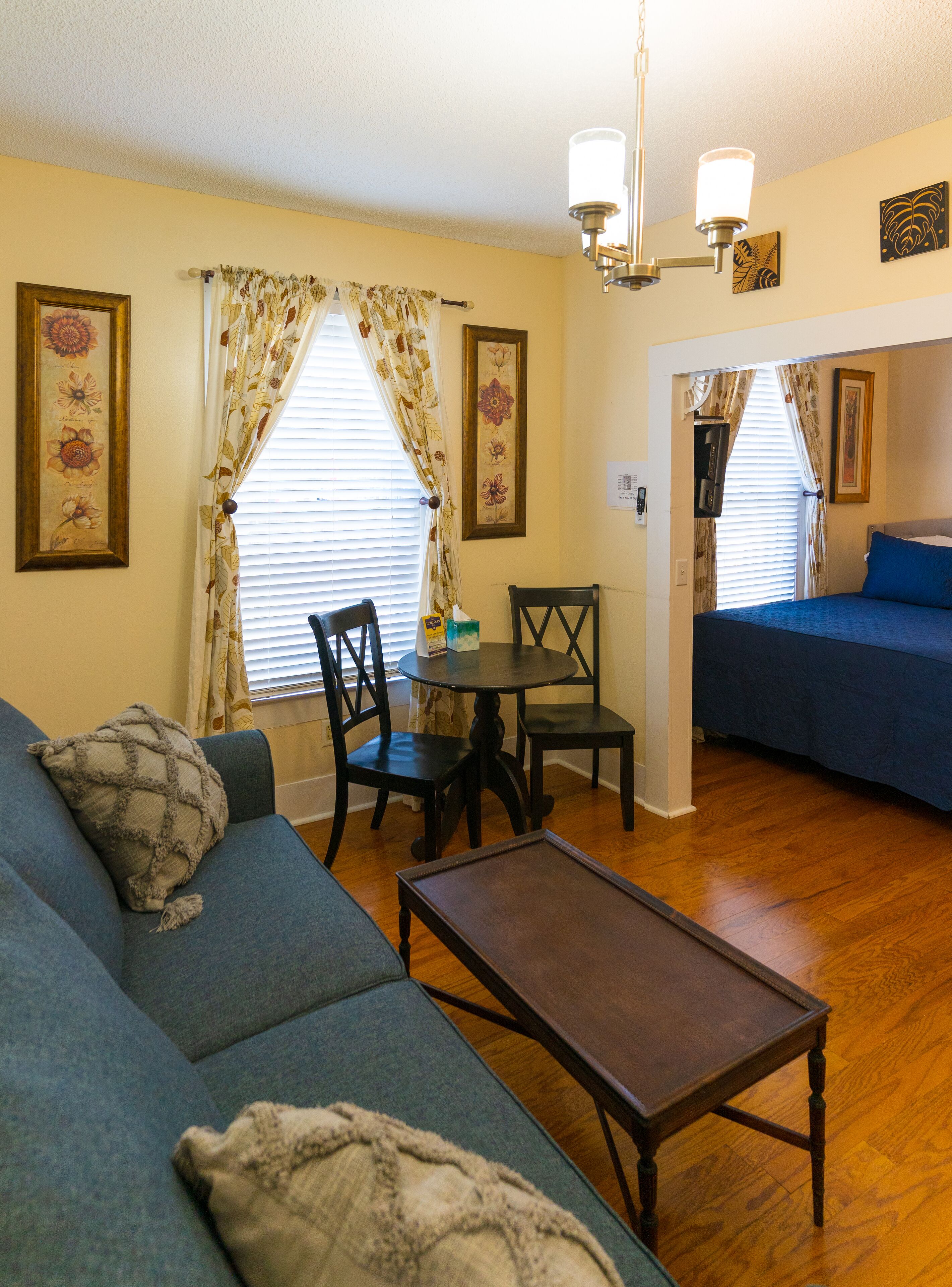 A cozy living room with a blue sofa, a wooden coffee table, and a dining area with a small table and chairs.