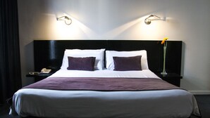Una cama bien hecha con ropa de cama blanca y morada, un cabecero negro y dos lámparas de noche.