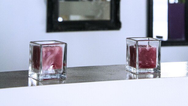 Una habitación con un espejo, cuadros enmarcados y dos velas sobre una mesa.