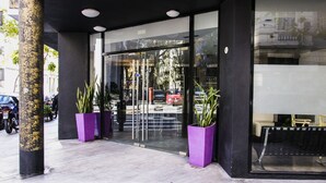 Entrada de un edificio moderno con puertas de vidrio, fachada negra y dos macetas moradas.