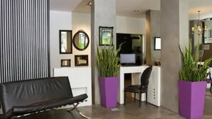 Zona de recepción con un sofá de cuero negro, un escritorio con computadora y dos grandes macetas moradas.