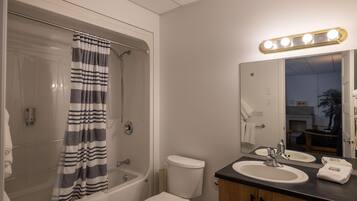 A bathroom with a bathtub, toilet, and vanity with a mirror and lights.