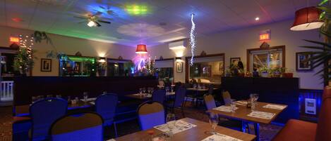 Un restaurante con cabinas y mesas, ventiladores de techo e iluminación decorativa.