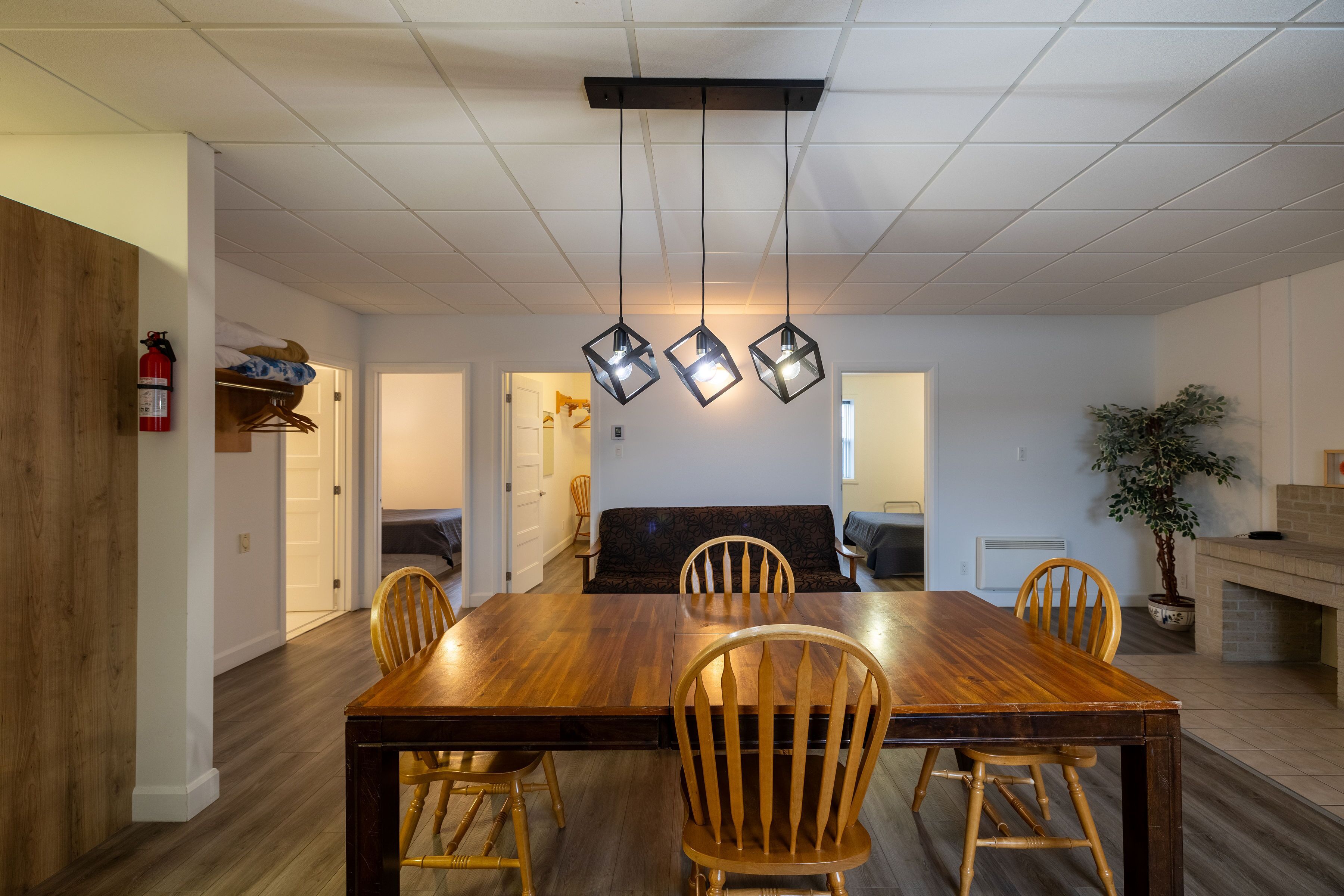 Un espace repas comprenant une table et des chaises en bois, un banc intégré, des luminaires suspendus et une plante en pot.