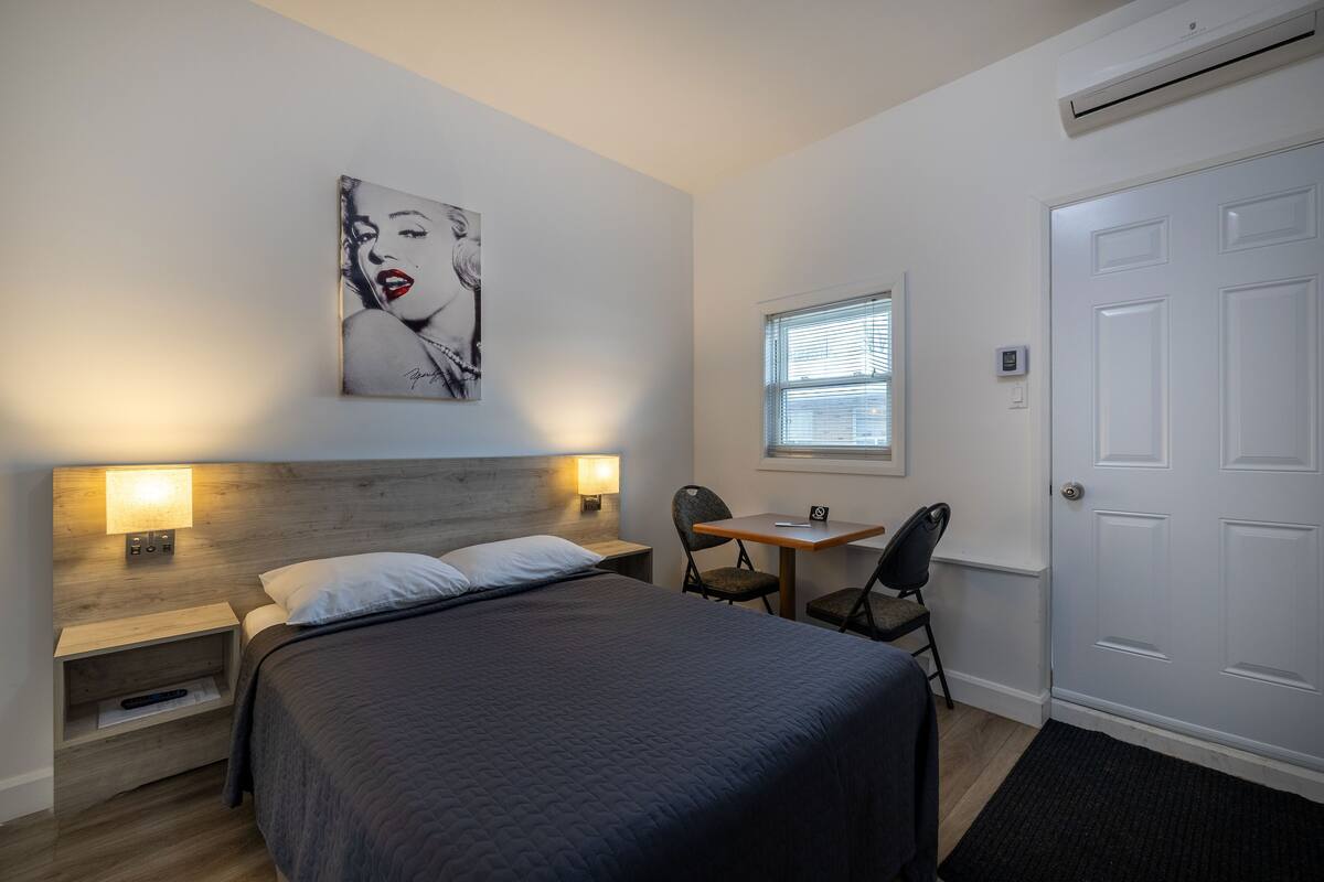 A bedroom with a bed, bedside tables, a desk, a chair, a window, and a door.