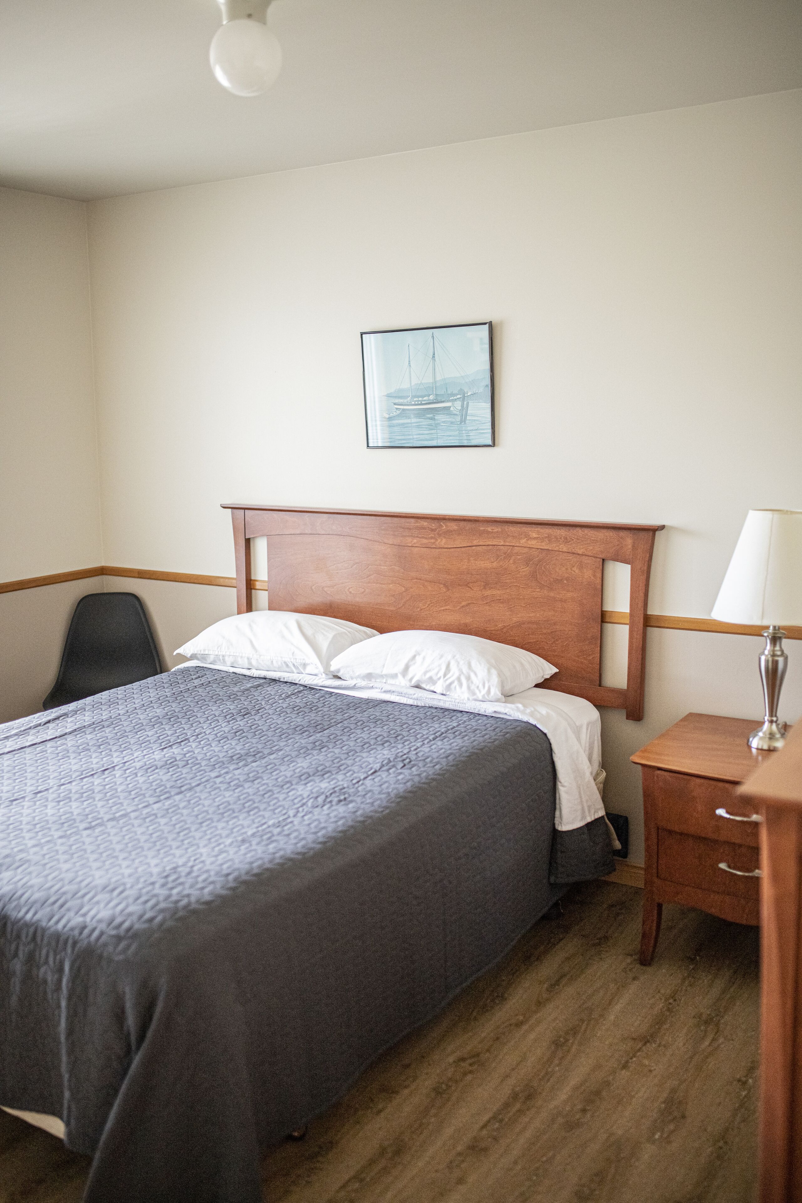 A neatly made bed with a wooden headboard, a bedside table with a lamp, and a framed picture on the wall.