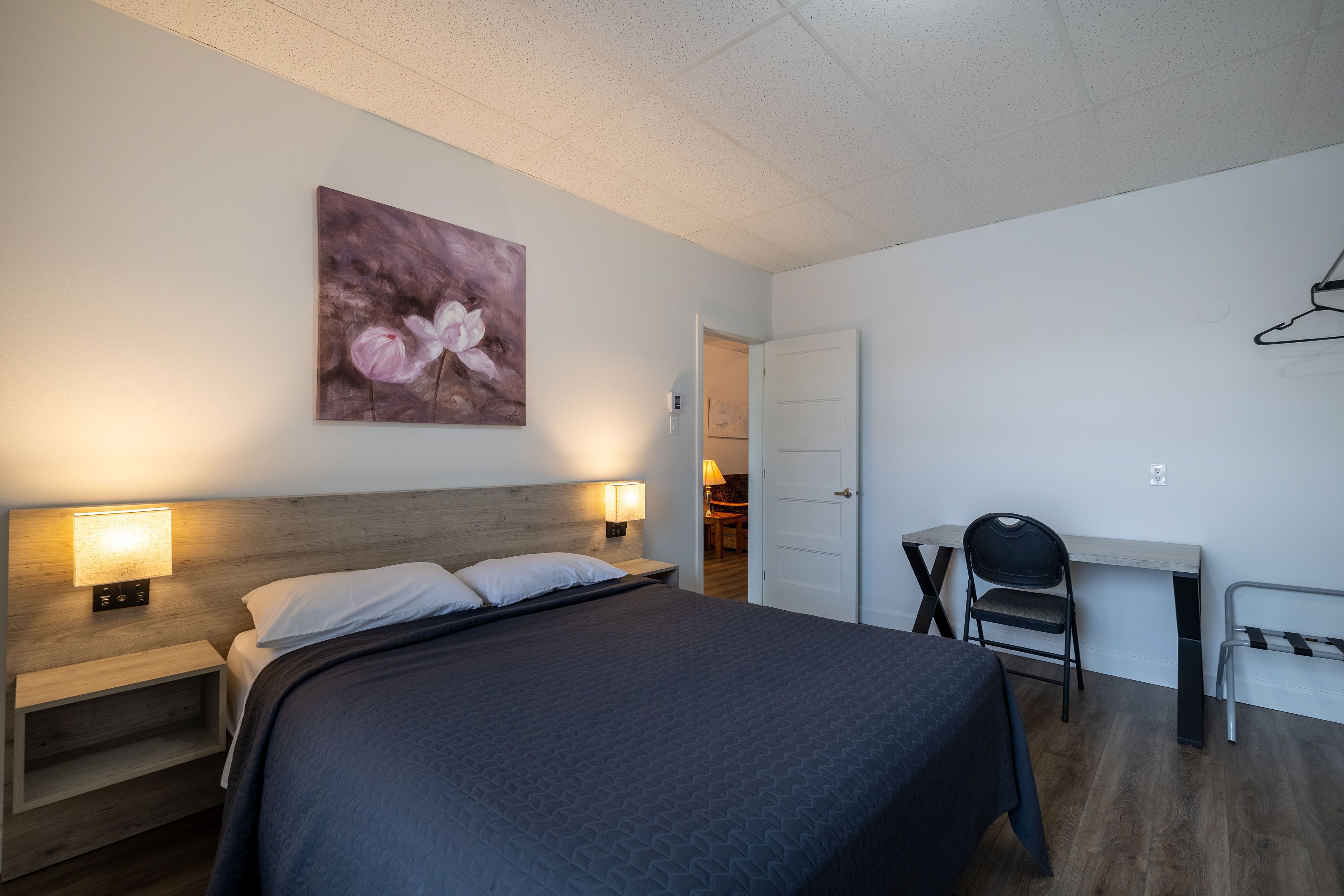 Quarto com cama, mesas de cabeceira, escrivaninha e uma cadeira.