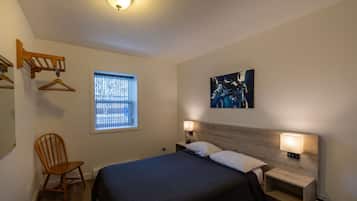 A bedroom with a bed, a chair, a window, and a wall-mounted lamp.