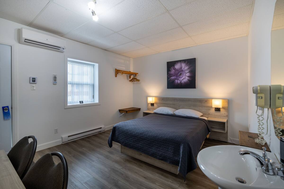 A hotel room with a bed, bedside table, lamp, and a bathroom with a sink and mirror.