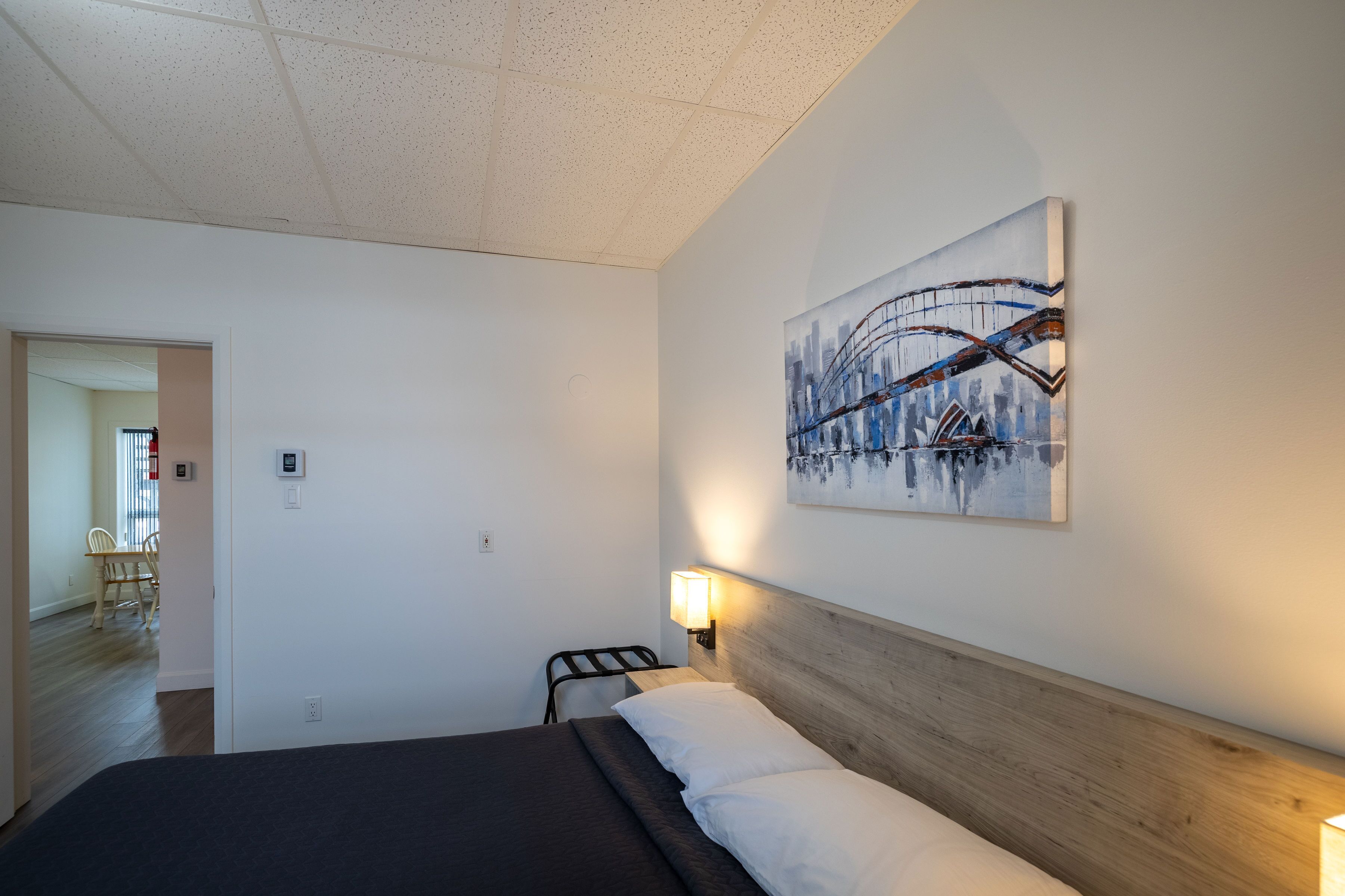 A hotel room with a bed, a headboard, a wall-mounted light, and a painting.