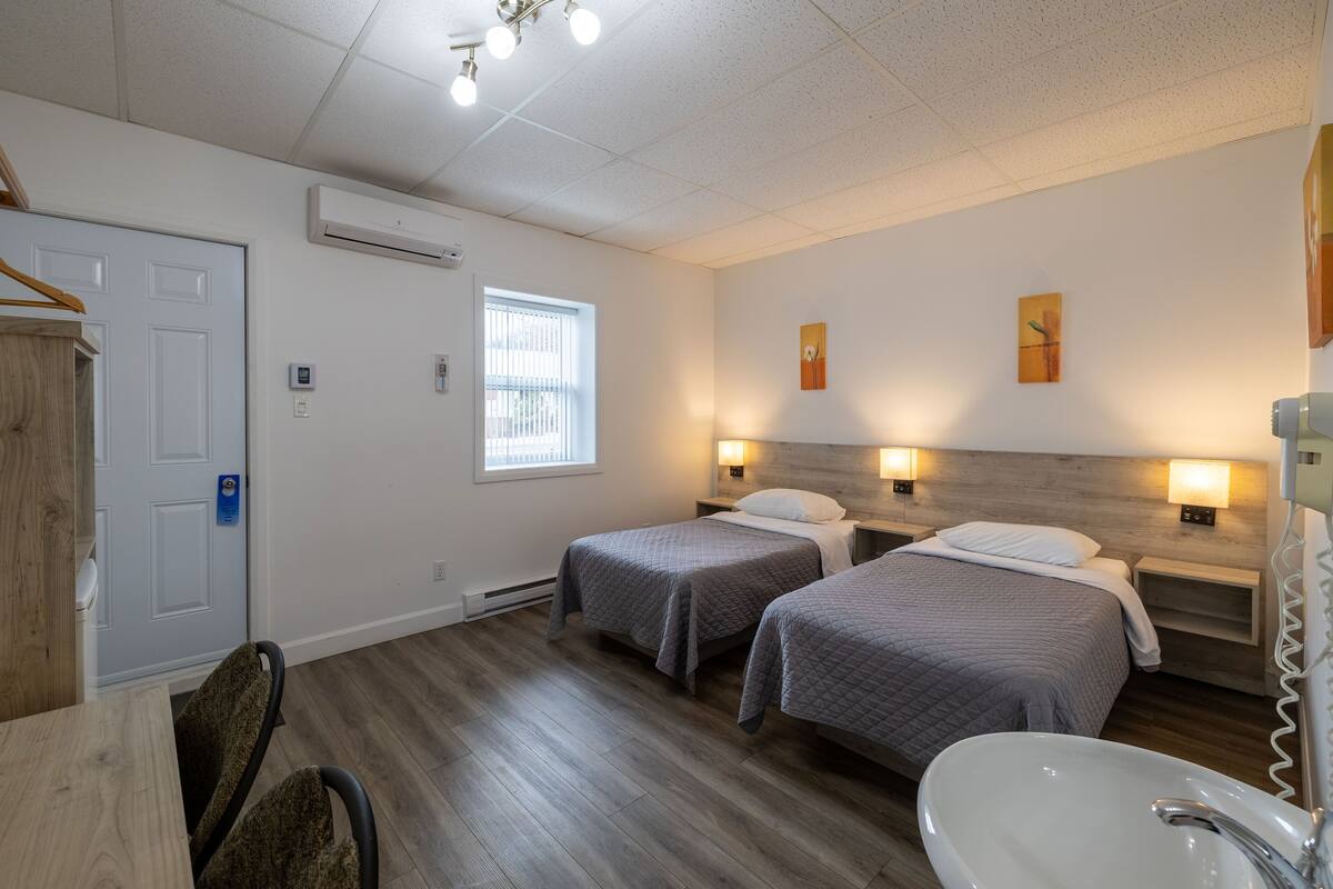A hotel room with two beds, a desk, a chair, a sink, and a window.