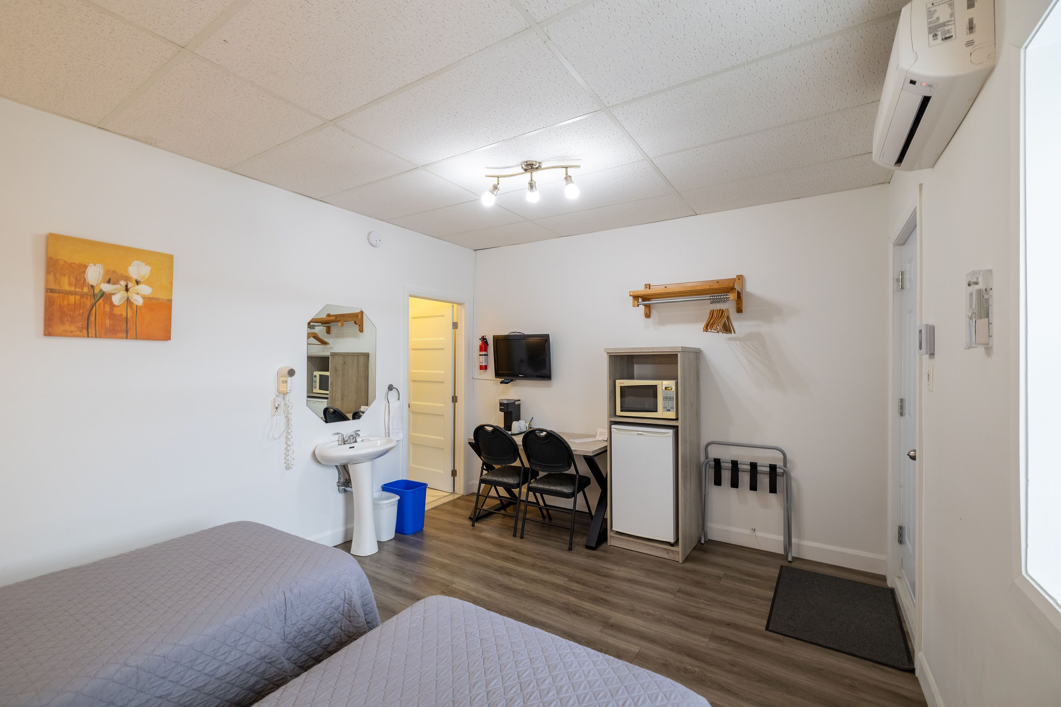 A room with two beds, a desk with a chair, a sink, a mirror, a microwave, and a TV.