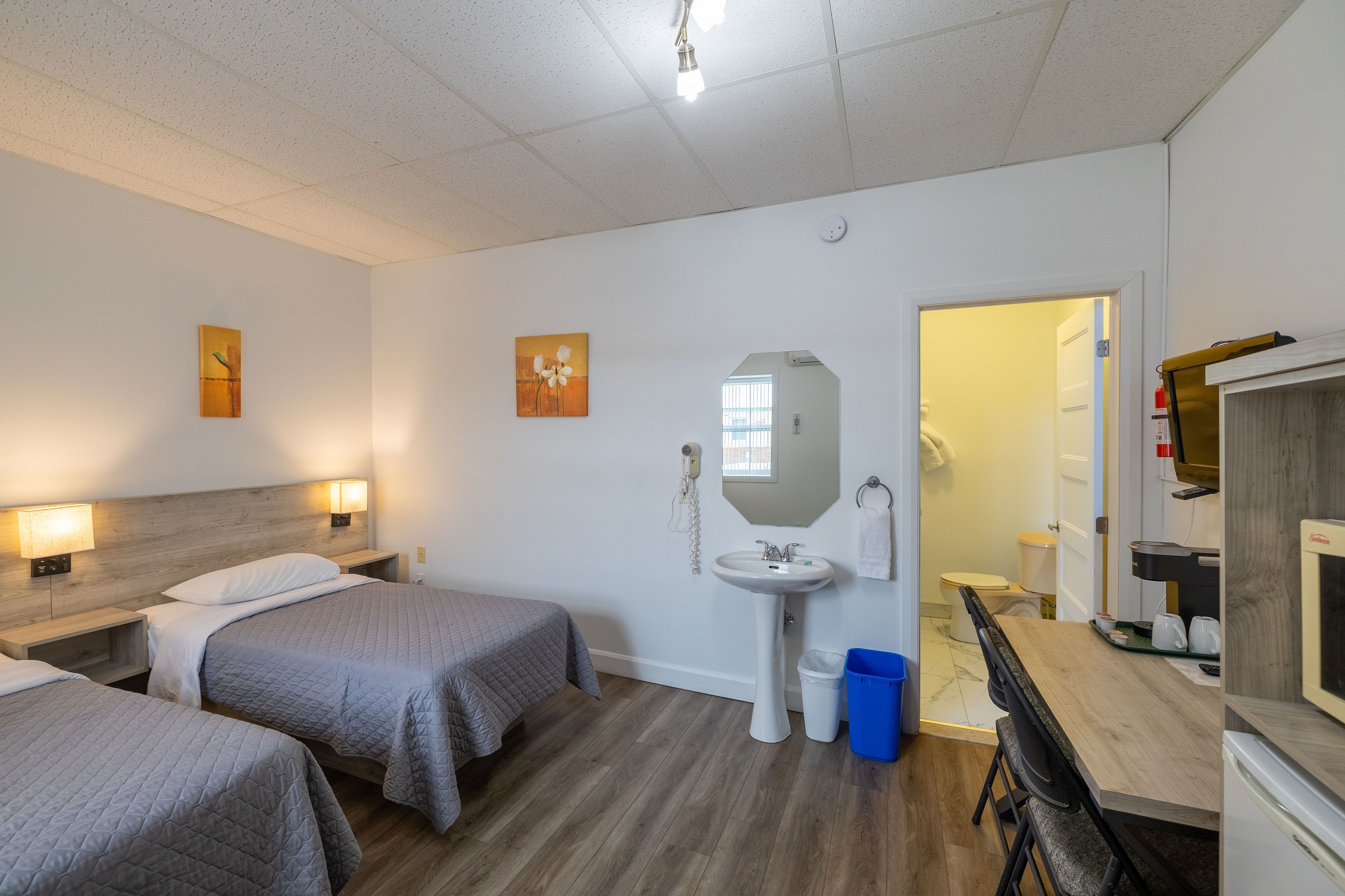 A hotel room with two beds, a sink, a mirror, a desk, and a kitchenette.