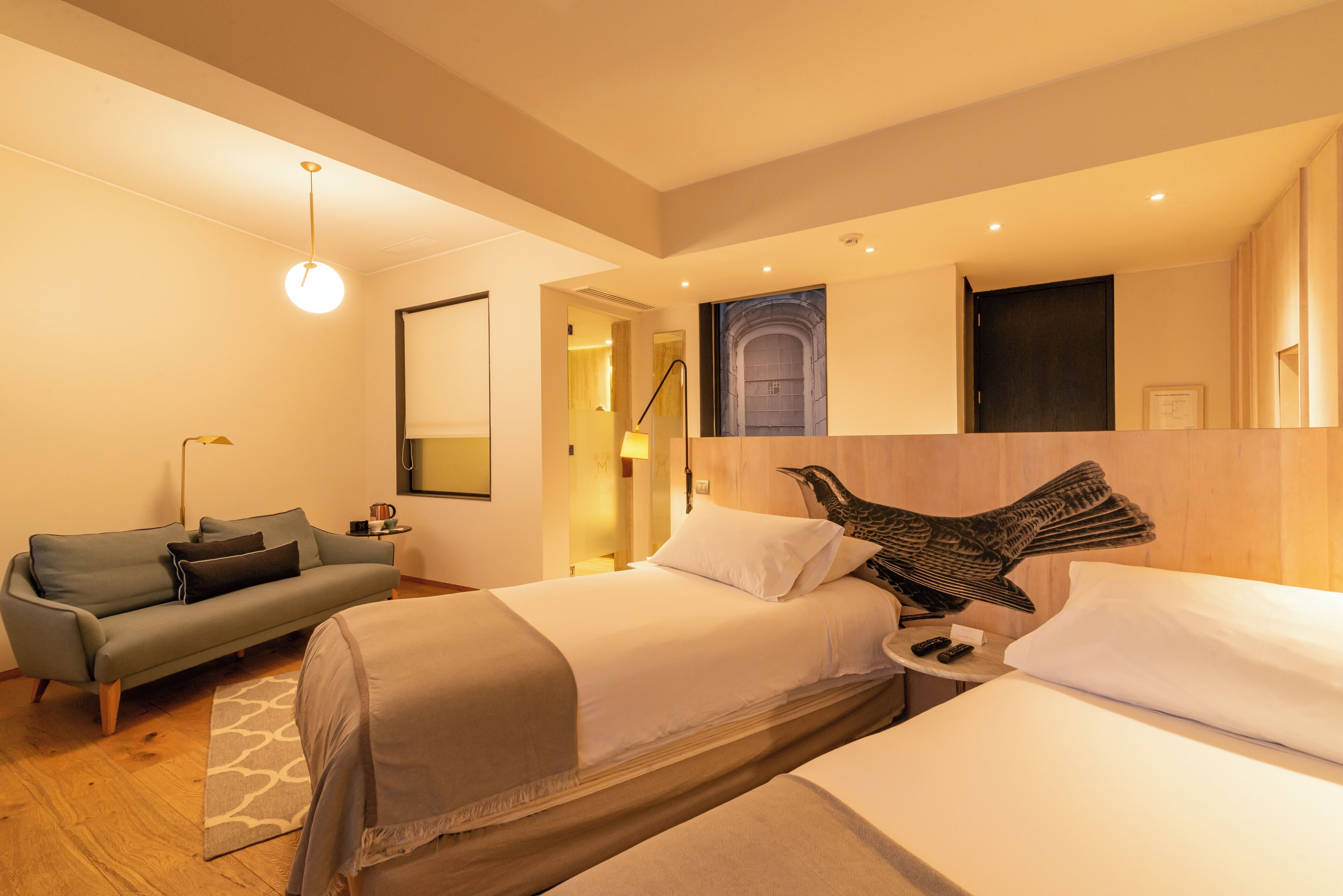 Camera d'albergo con due letti, un divano, una lampada e un'opera d'arte appesa al muro.