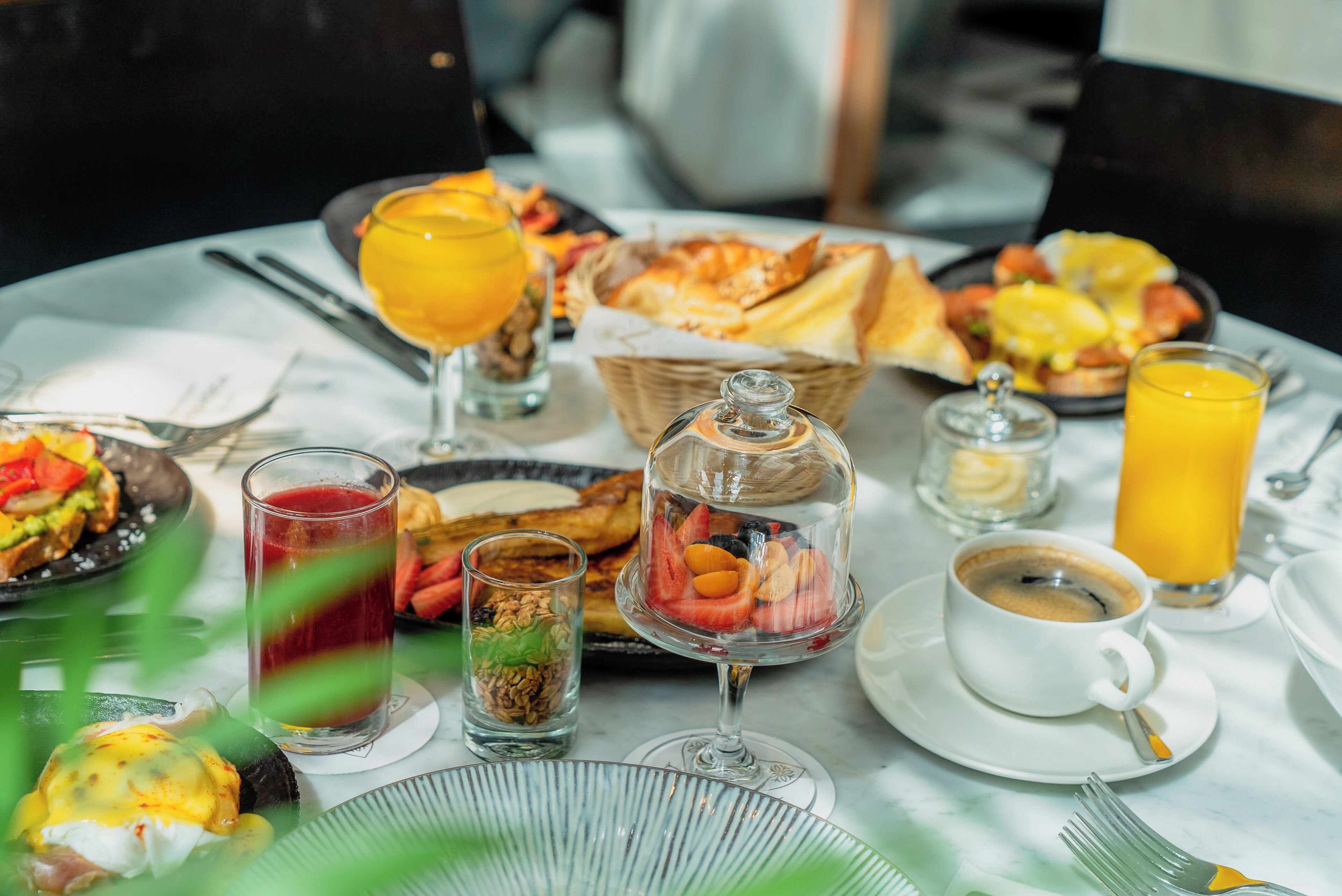 A breakfast setting with various dishes, drinks, and a basket of bread.