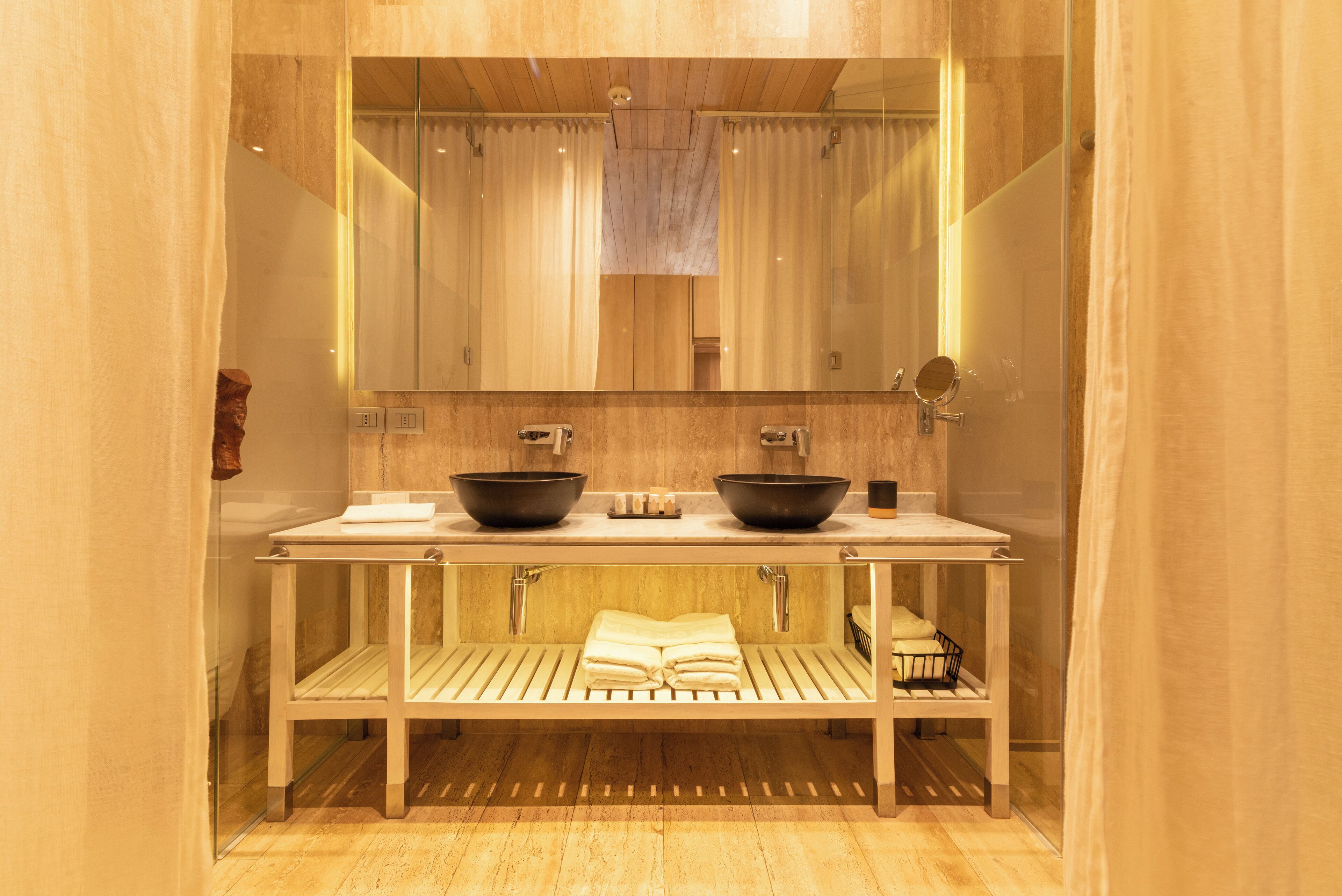 A modern bathroom with a wooden vanity, two black bowls, a mirror, and a towel rack.