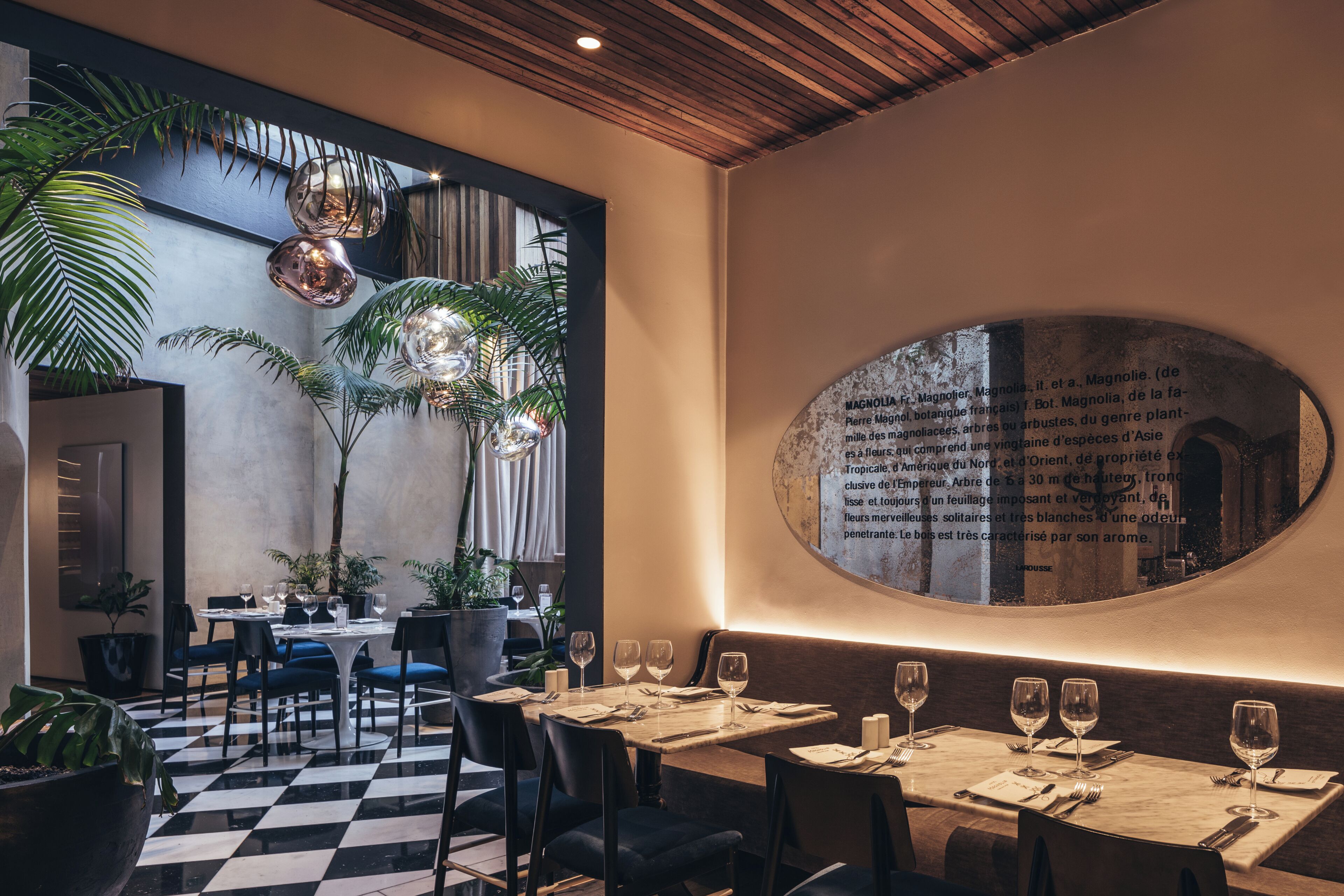 Un restaurante con suelo a cuadros, mesas redondas y plantas en macetas.