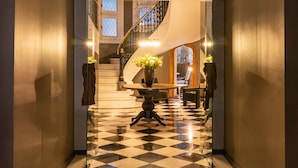 Un pasillo con piso a cuadros que conduce a una escalera con barandilla de cristal.