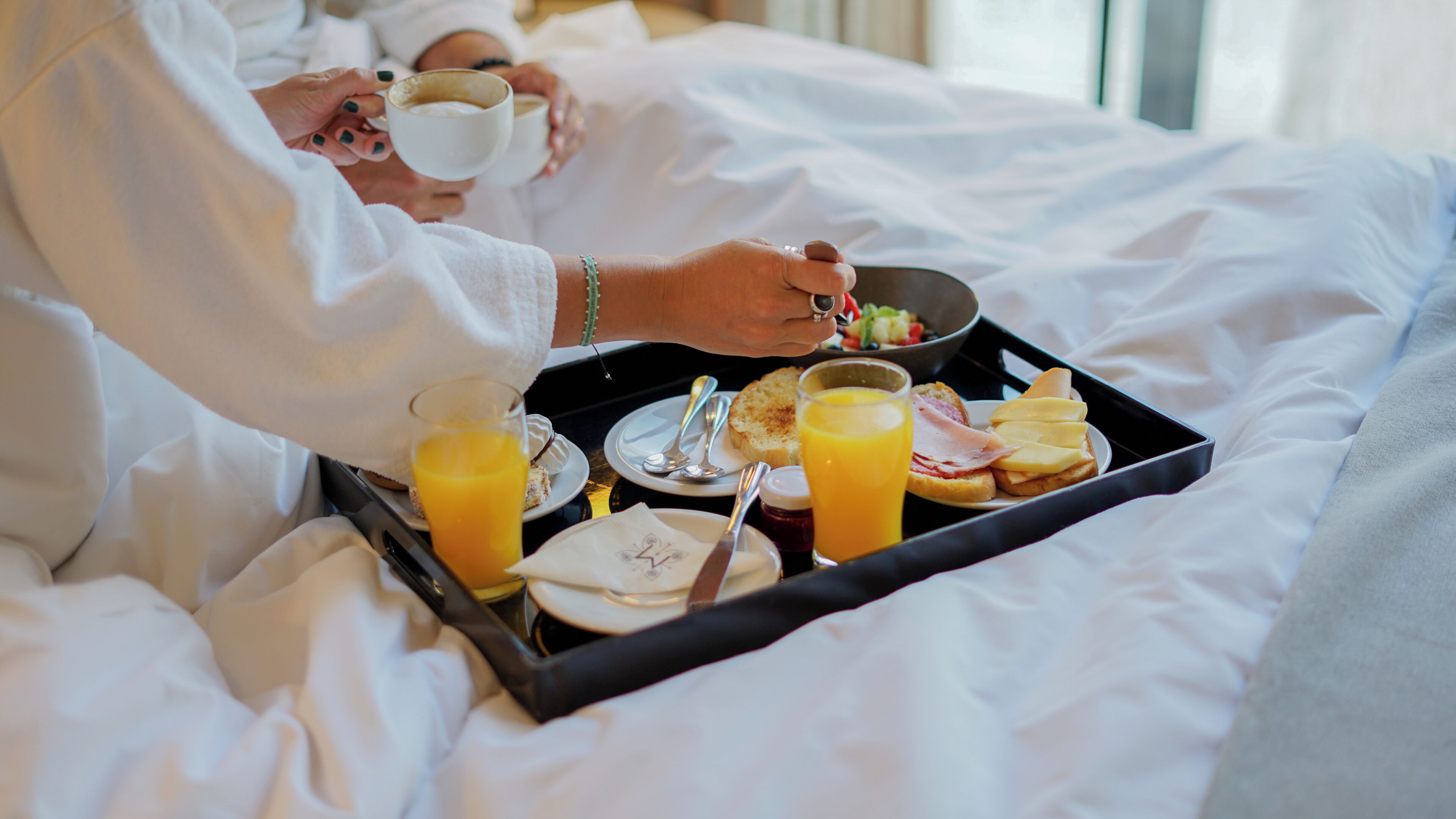 Bandeja de desayuno con tostadas, jamón, queso y zumo de naranja sobre la cama.