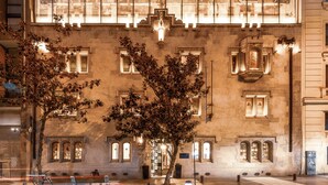 Un edificio moderno con fachada de vidrio, un árbol en el frente y una plaza pavimentada.