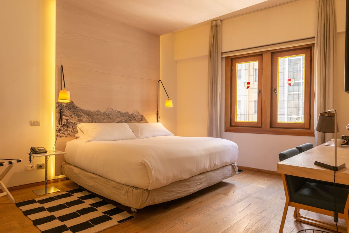 A bedroom with a bed, bedside lamps, a desk, and a window with curtains.