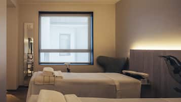 Two beds and a bedside table in a minimalist room with a large window and a wall-mounted telephone.