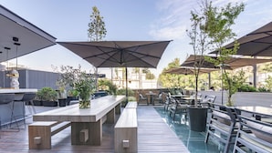 Un patio al aire libre con mesas y bancos de madera, sombrillas y plantas en macetas.