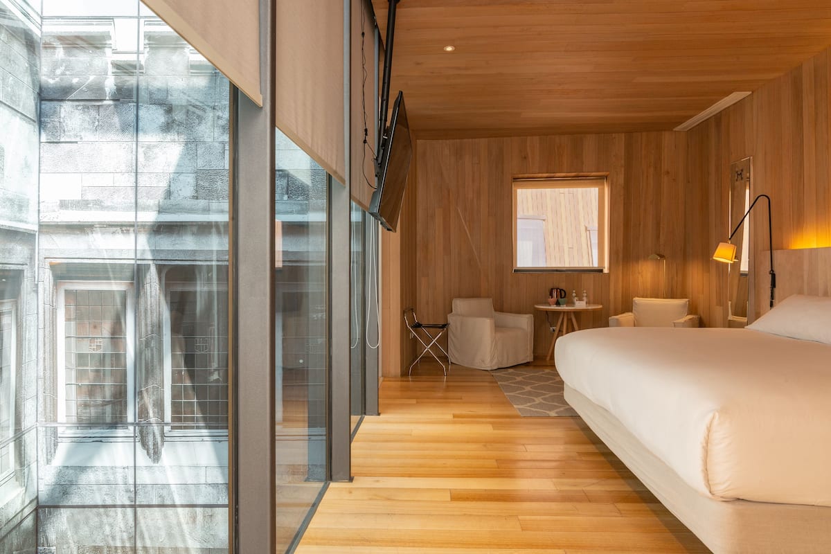 A modern hotel room with a large bed, a small desk, a chair, a window, and a view of the outside.