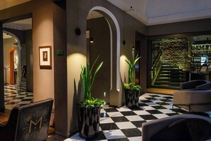 A lobby with a checkered floor, potted plants, a framed portrait, and a staircase with a stone wall. - Hotel Magnolia (Santiago)