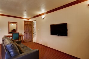 Una sala de estar con un sofá de cuero, un televisor montado en la pared y una puerta de madera que da a otra habitación.