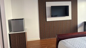 Une chambre d’hôtel avec un lit, un téléviseur fixé au mur, qui est recouvert d’un panneau en bois, et un petit téléviseur posé sur un meuble.