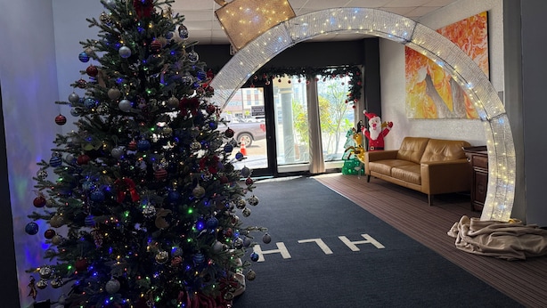 Un sapin de Noël décoré de guirlandes et de lumières, un canapé en cuir et un panneau avec les lettres « H » posé sur le sol.