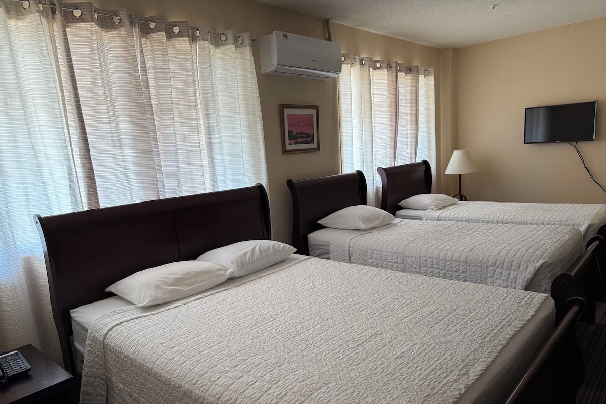 A hotel room with two beds, a flat-screen TV, an air conditioner, and a telephone on a nightstand.