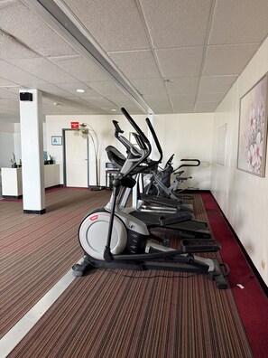 A gym with multiple treadmills lined up against a wall with a red carpet, a white ceiling, and a door labeled 'EMPLOYEE'.
