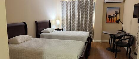 A hotel room with two beds, a desk, a chair, a lamp, a TV, and a window with curtains.