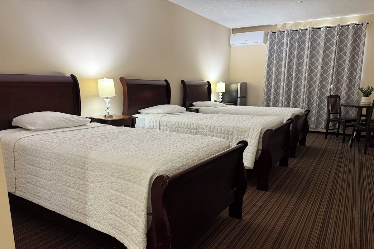 A hotel room with two beds, a desk, a chair, a lamp, and a window with curtains.